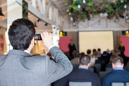 Man takes a picture of the presentation at the conference hall using smartphone.view eventの写真素材