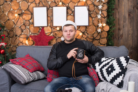 young man in a Santa Claus hat sits on the couch with a camera