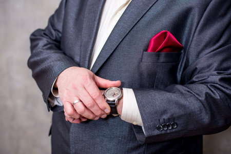 Business man adjusting his watch, on a grey background.