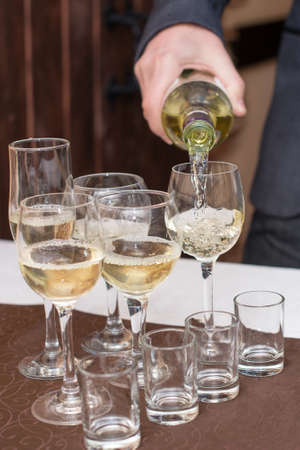 Mans hand pours champagne, white wine from bottle in wineglasses on tableの写真素材