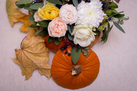 Autumn floral bouquet in a pumpkin vase on a light background, a mixture of flowers, pionic rose, eucalyptus, chrysanthemum.の写真素材