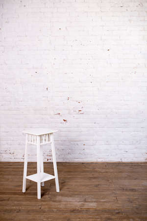 White bar stool on wooden floor against white brick wall.の写真素材