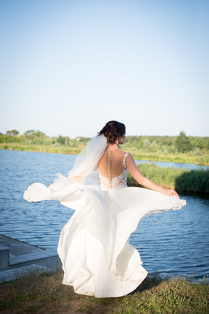 Woman face beauty. Woman waving wedding dress as wings. Girl standing on green grass, back view. Bride on sunny day on tropical landscape. Honeymoon and summer vacation. Beauty and fashion concept.の写真素材