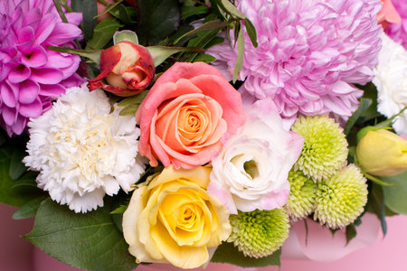 beautiful floral arrangement in the box, pink and yellow rose, pink eustoma, green and pink chrysanthemum, white carnation, pink dahlia on pink background with space for text.の写真素材