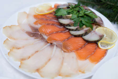Fresh slices of salmon, red fish and herring on a white plate in a restaurant. Fish platter is decorated with slices of fresh lemon, herbsの写真素材