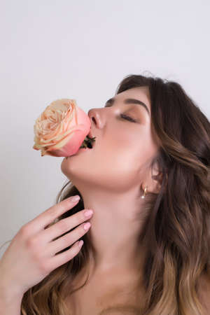 Beautiful brunette woman with red lipstick on lips. Close-up girl with beautiful make-up. Woman with dark hair is posing and holding a rose in her mouth.の写真素材