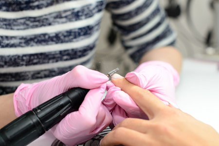 Closeup shot of a woman in a nail salon receiving a manicure by a beautician with electric nail file. Woman getting nail manicure. Beautician file nails to a customer.の写真素材