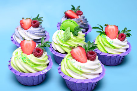 cupcakes with whipped cream decorated chocolate bar, strawberry ,macaroons on blue background. Picture for a menu or a confectionery catalog. with space for textの写真素材
