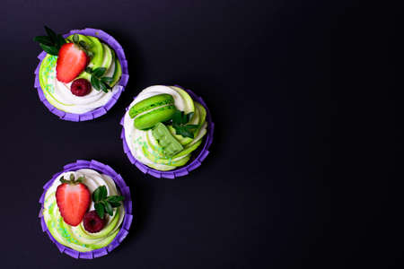 cupcakes with whipped cream decorated chocolate bar, strawberry ,macaroons on black background. Picture for a menu or a confectionery catalog. with space for textの写真素材
