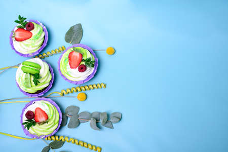 cupcakes with whipped cream decorated chocolate bar, strawberry ,macaroons on blue background. Picture for a menu or a confectionery catalog. with space for text. decorated with eucalyptus leavesの写真素材