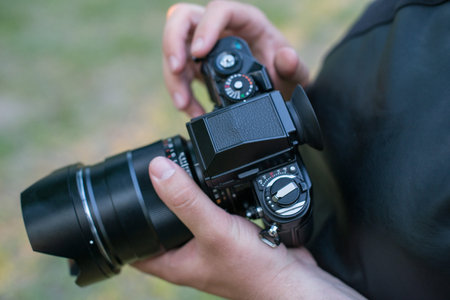 Closeup of a black camera holding by mans hand with natrural blackground in sunny day.