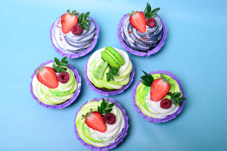cupcakes with whipped cream decorated chocolate bar, strawberry ,macaroons on blue background. Picture for a menu or a confectionery catalog. with space for text.の写真素材