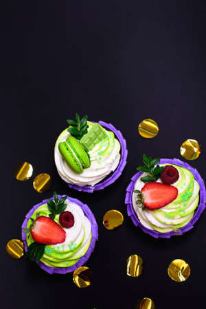 cupcakes with whipped cream decorated chocolate bar, strawberry ,macaroons on black background. Picture for a menu or a confectionery catalog. with space for textの写真素材