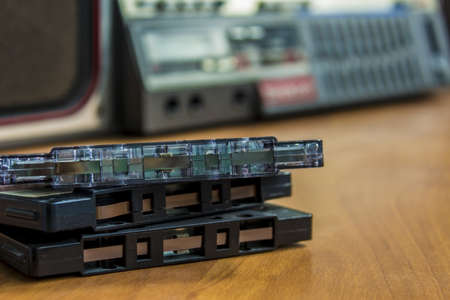 old vintage tape audio cassettes lying on wood surface with retro tape recorder on backgroundの写真素材