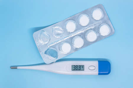 digital thermometer showing high temperature and tablets on blue background. High quality photoの写真素材
