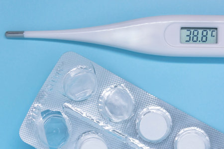 digital thermometer showing high temperature and tablets on blue background. High quality photo
