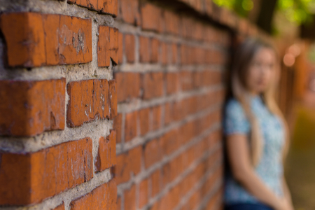 Blured girl standing near the brick wall and waiting. Blured backgroundの写真素材