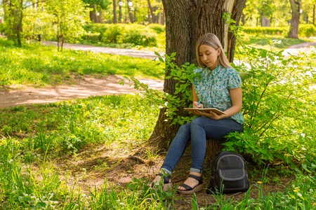 young woman writing in her diary on the grass in the parkの写真素材