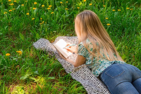 Beautiful woman writing in her diary on the grass with flowers. Rear view.の写真素材