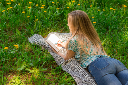 young woman writing in her diary on the grass with flowers. Rear view.の写真素材