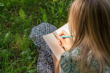 woman writing in her diary on the grass with flowers. Rear view.の写真素材
