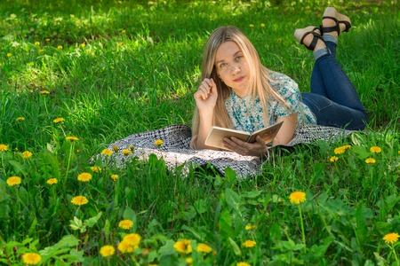 Beautiful young woman lying and writing in her diary on the grass with flowers. Front view.の写真素材