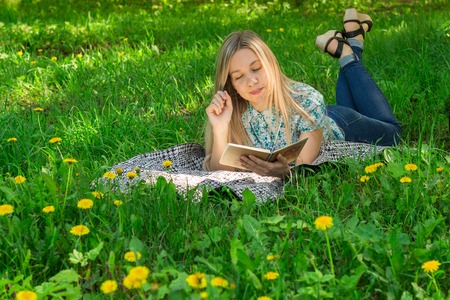 Beautiful woman lying and writing in her diary on the grass with flowers. Front view.の写真素材