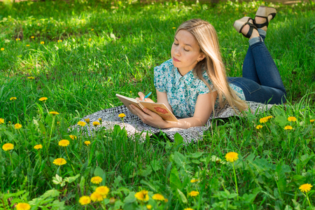 young woman lying and writing in her diary on the grass with flowers. Front view.の写真素材