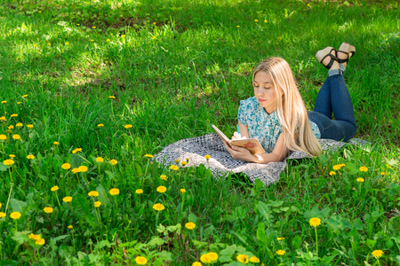 young woman thinking and writing in her diary on the grass with flowers. Front view.の写真素材