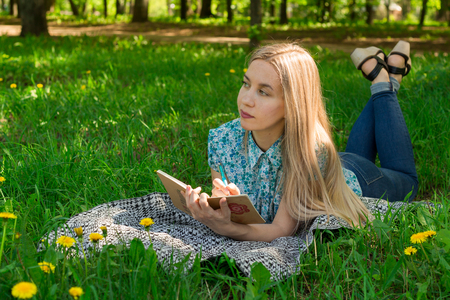 Beautiful girl thinking and writing in her diary on the grass with flowers. Front view.の写真素材