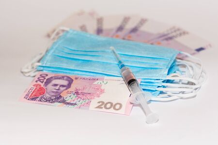 Protective medical mask, syringe vaccine and Ukrainian hryvnia. Expensive medicine concept.の写真素材