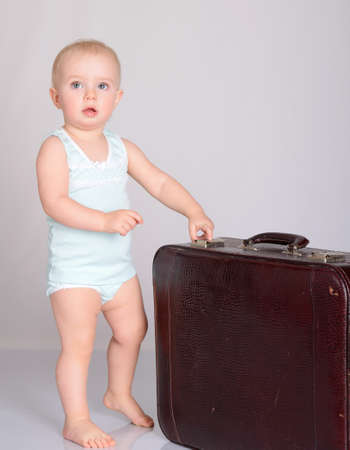 cute baby girl playing with suitcase on grey backgroundの写真素材