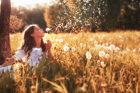 girl in white dress blow dandelion in outdoor