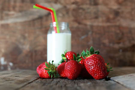 wooden table with strawberries and milk in a glassの写真素材