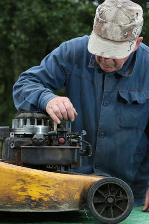 old man repairing lawn mower engine outdoorの写真素材