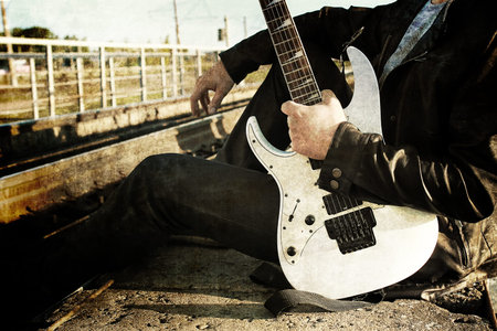 a young man in a leather biker jacket with electric guitar on the street in spring day