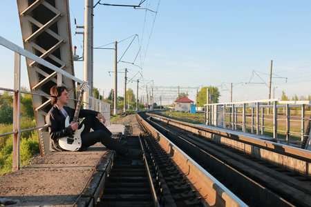 a young man in a leather biker jacket with electric guitar on the street in spring dayの写真素材