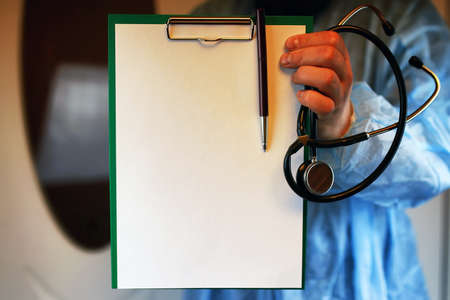 Doctor in blue robe holding a tablet for notes and a stethoscope in the hands ofの写真素材