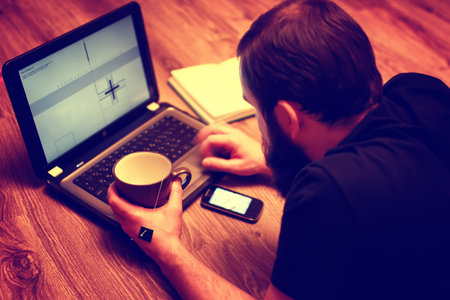 bearded handsome man lies on the floor wrapped in a plaid, and working at a laptopの写真素材