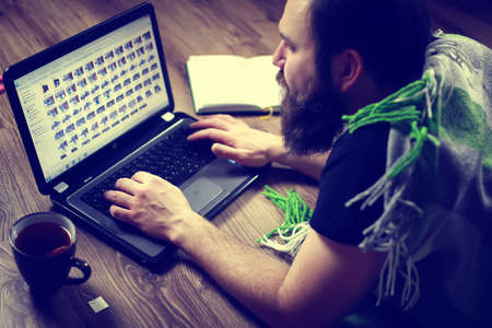 bearded handsome man lies on the floor wrapped in a plaid, and working at a laptopの写真素材