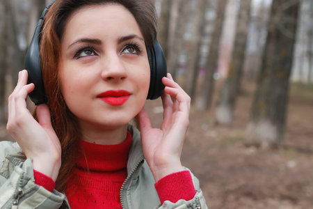 good-looking student listening to music on headphones walking through autumn park of tall treesの写真素材