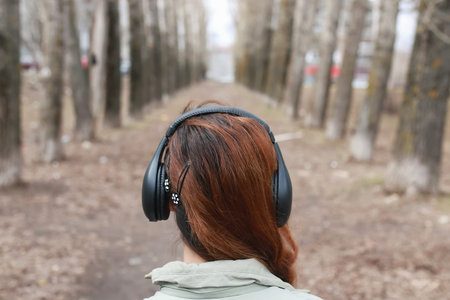 good-looking student listening to music on headphones walking through autumn park of tall trees