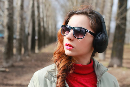 good-looking student listening to music on headphones walking through autumn park of tall trees