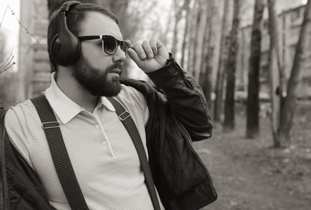 good-looking student listening to music on headphones walking through autumn park of tall treesの写真素材