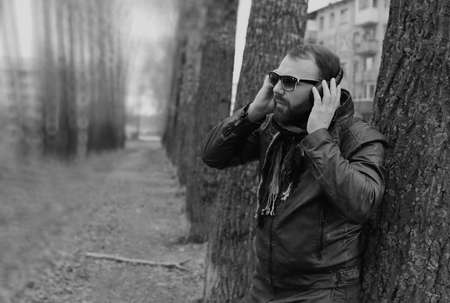 good-looking student listening to music on headphones walking through autumn park of tall treesの写真素材