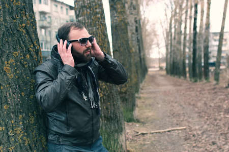 good-looking student listening to music on headphones walking through autumn park of tall treesの写真素材