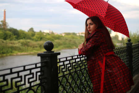 beautiful girl in a red raincoat with an umbrella walks in the rainの写真素材