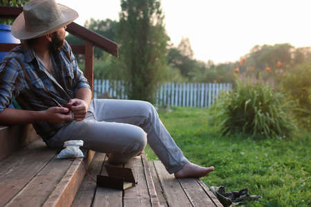 beard man with cowboys hat holding smoke pipe sitting at outdoor during sunsetの写真素材