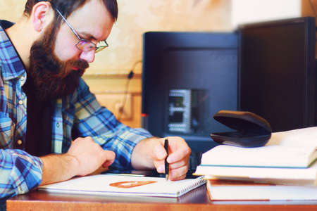bearded man sitting at a table and working with a laptopの写真素材