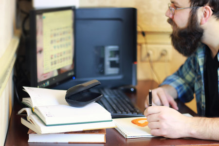 bearded man sitting at a table and working with a laptopの写真素材